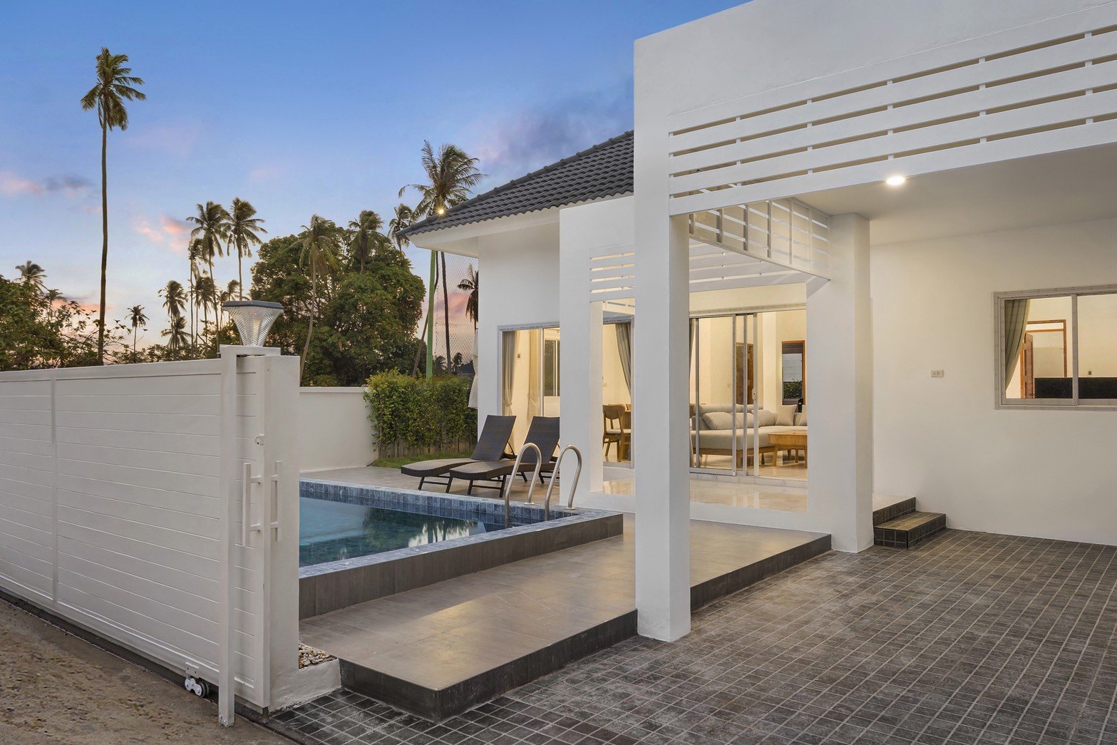 A finished villa at dusk, the pool and terrace lit in front of the living room