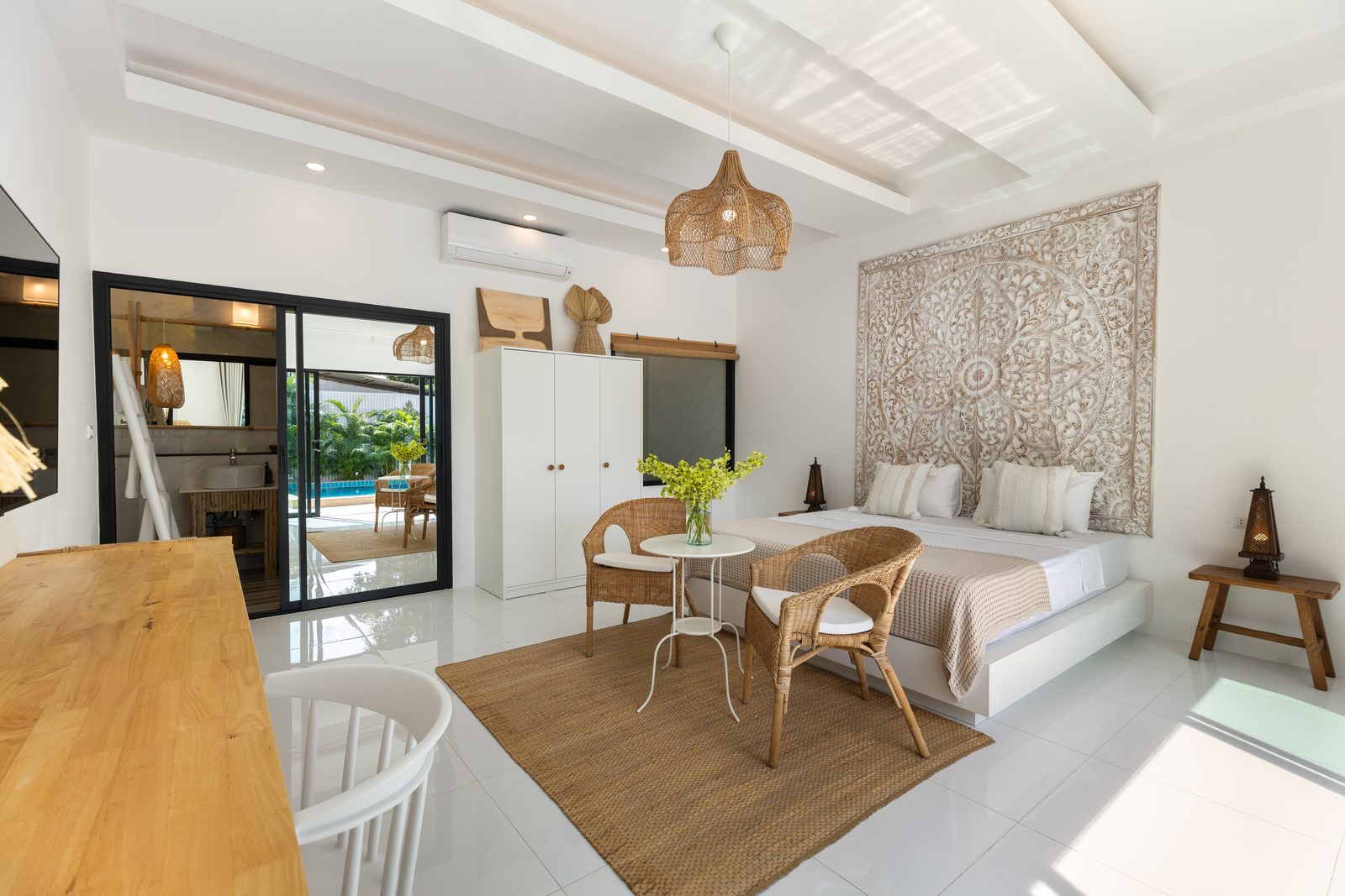 A bedroom with a carved timber headboard, opening onto the pool