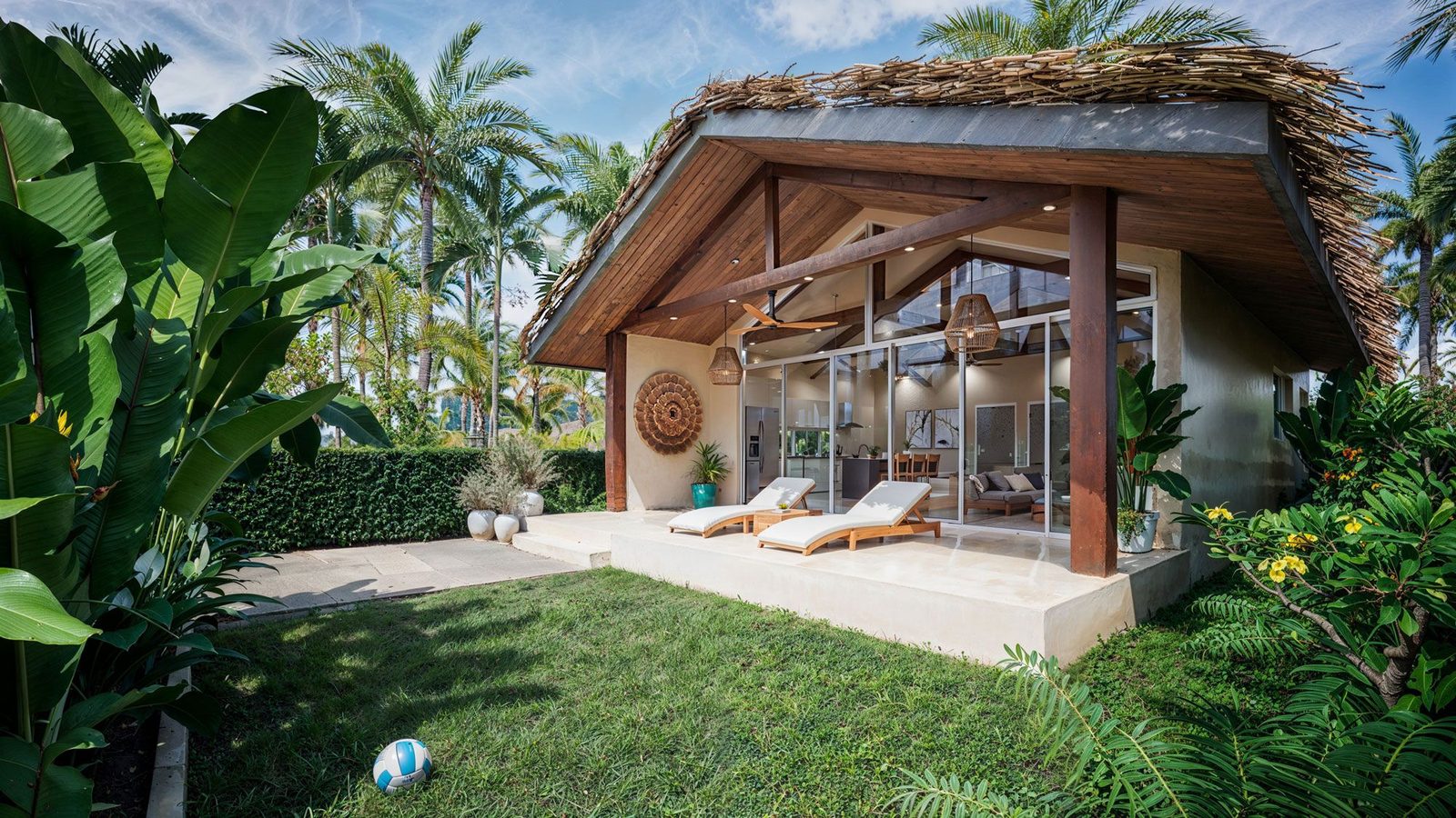 Villa exterior with lawn, sun loungers and thatched roof