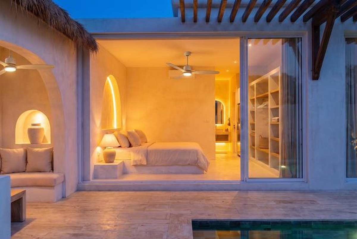 Bedroom at night, a lit niche behind the bed and the pool outside
